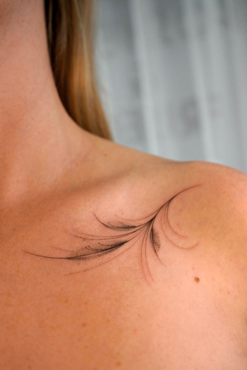 A wispy feather tattoo on the collarbone