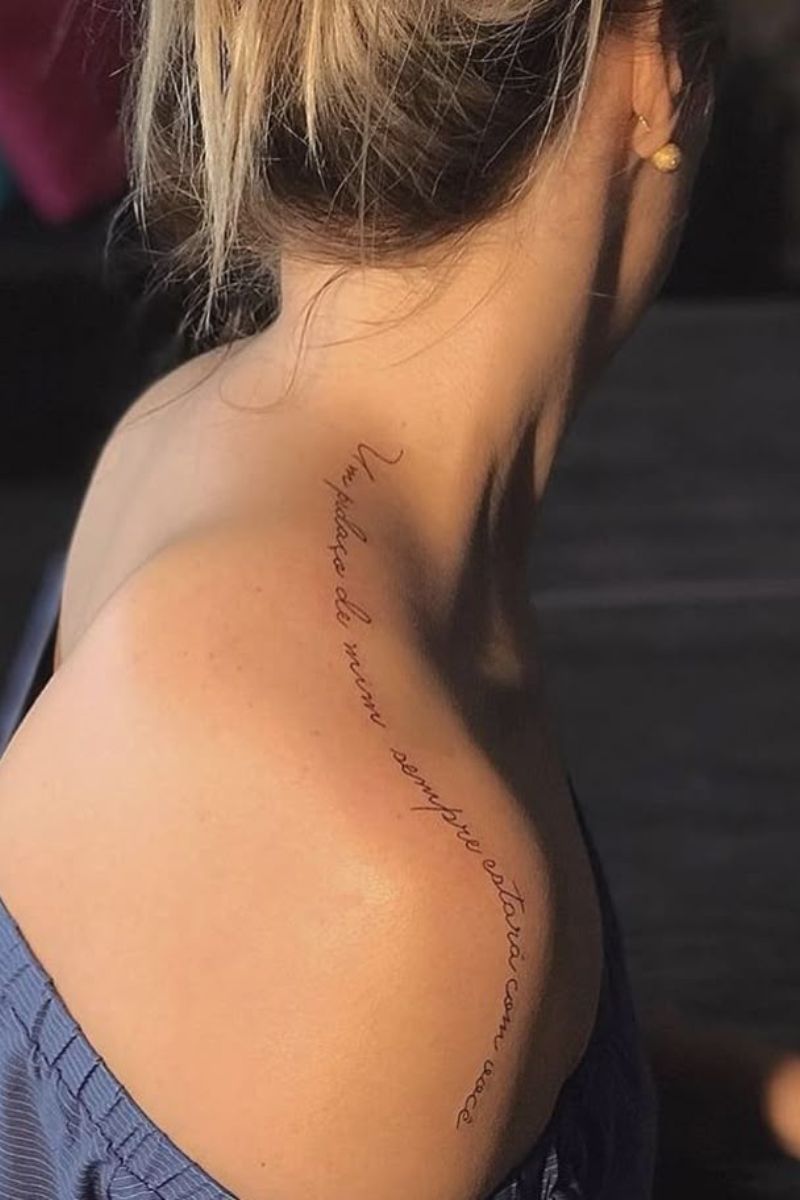 A linear quote tattoo all along the top of a woman's shoulder