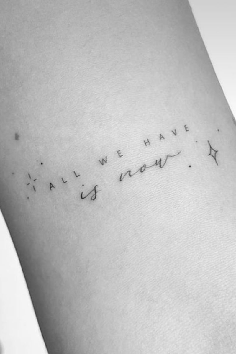 A black and white photo of a tattoo that says "all we have is now" in a small font