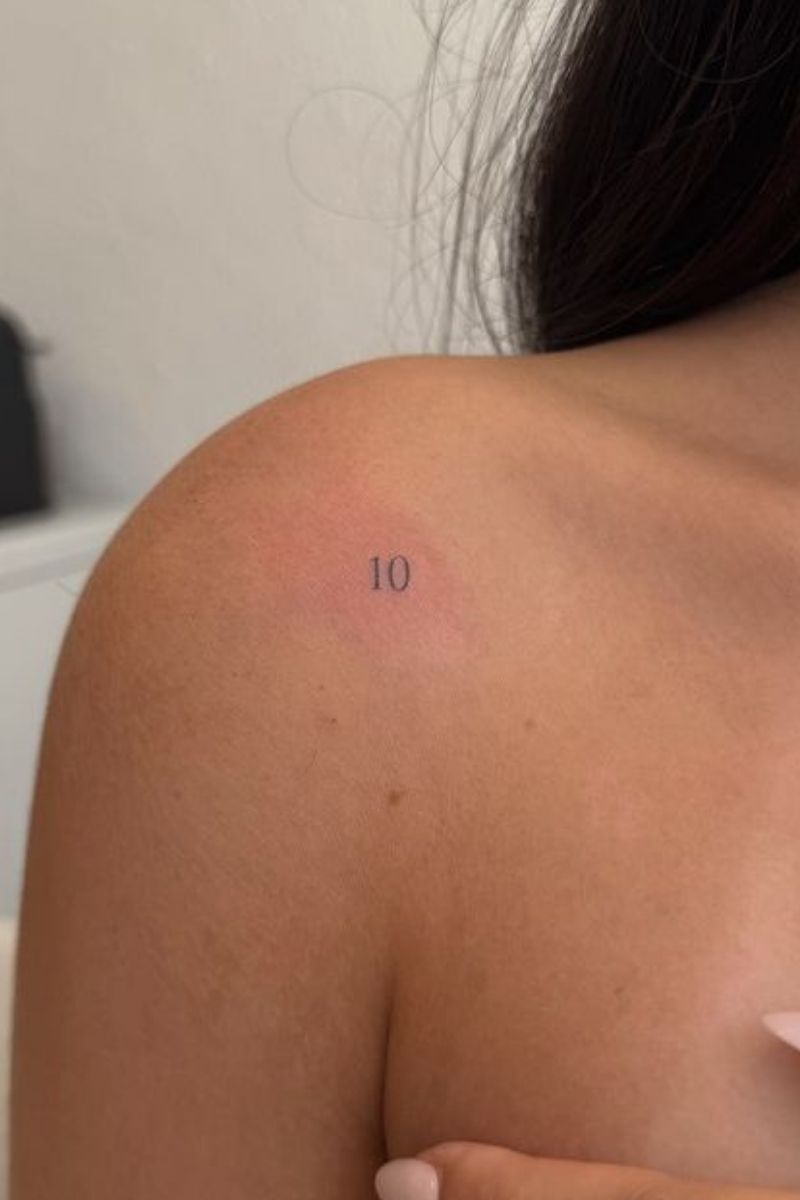 A tiny tattoo of the number "ten" on a woman's shoulder